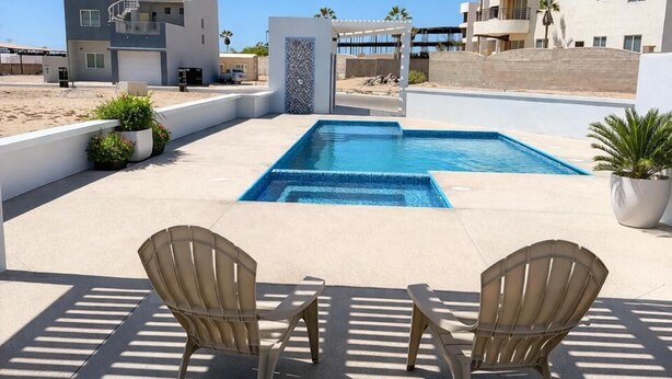 A pool area with two chairs, a pergola, and buildings in the background. - Residence 4 (4 Bed 3.5 Bath By FMI Rentals) (Puerto Peñasco)