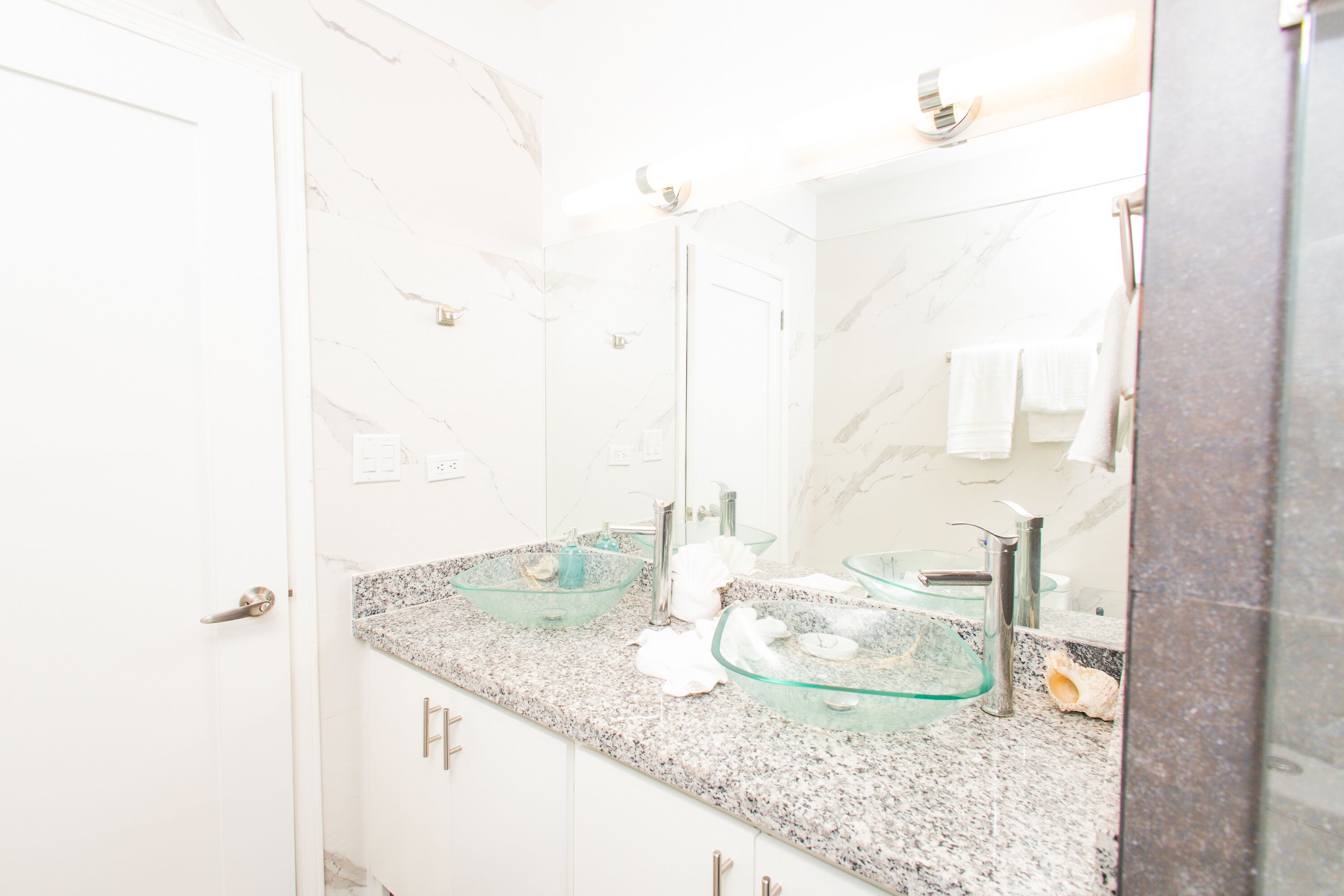 Un baño con pared de mármol, lavamanos de cristal y un espejo.