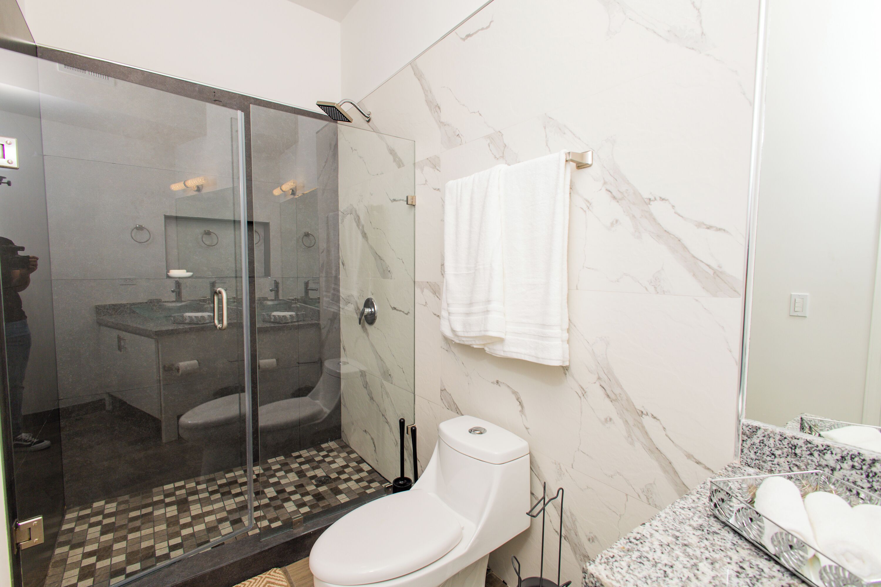 A modern bathroom with a glass-enclosed shower, a toilet, and a marble-tiled wall.