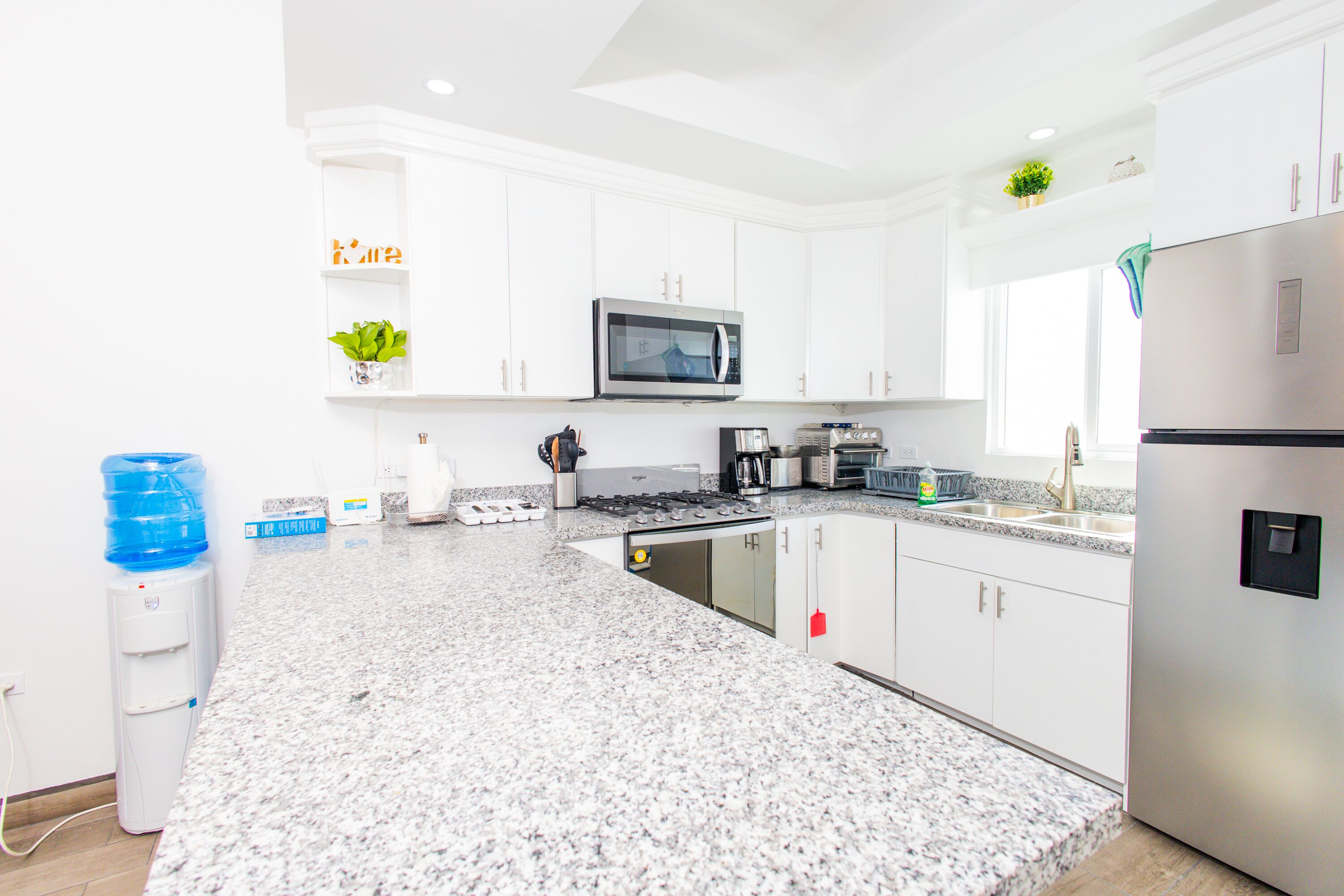 A modern kitchen with white cabinets, a stainless steel refrigerator, a microwave, and a water dispenser.
