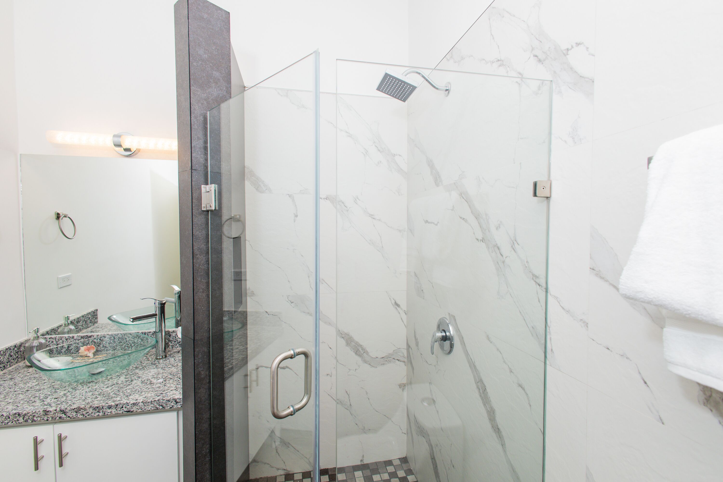 A modern bathroom with a glass shower enclosure, a marble-tiled wall, and a glass sink with a marble countertop.