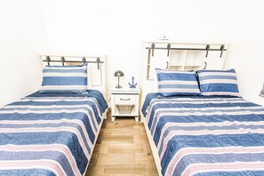 Quarto com duas camas, cada uma com roupa de cama listrada e mesa de cabeceira com abajur e um objeto decorativo pequeno.