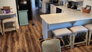 A modern kitchen with white cabinets, a central island with bar stools, a built-in oven, and a refrigerator. - Cottage at Lake Cumberland; 6m walk to water at Clearwater public boat ramp (Nancy)
