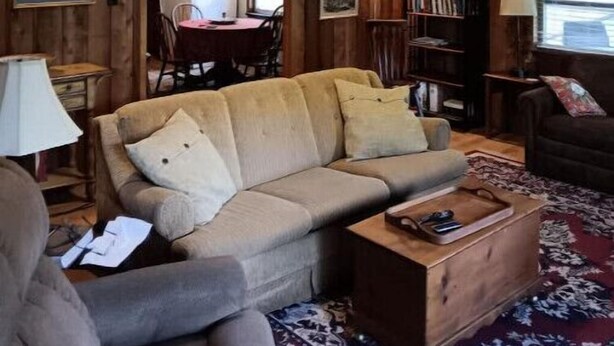 A cozy cabin interior with wooden walls, a sofa, a coffee table, and a bookshelf. - Twin Creeks on the Cullasaja (Franklin)