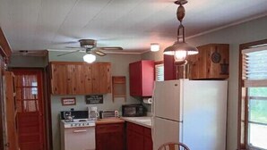 A compact kitchen with wooden cabinets, a white refrigerator, a stove, and a dining table with chairs. - Twin Creeks on the Cullasaja (Franklin)