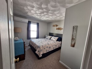 Un dormitorio con cama, mesita de noche, lámpara, ventana con cortinas y un cuadro decorativo de peces.