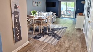 Un salon moderne comprenant un coin repas, un ensemble de canapés et un téléviseur fixé au mur.