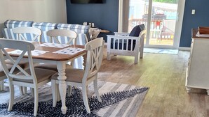 Un coin repas avec une table et des chaises, un téléviseur fixé au mur et une vue sur l’extérieur à travers une porte vitrée.