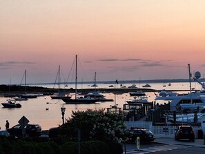 A marina with boats docked, a white fence, and a street with cars.