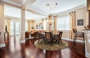 A spacious dining area with a round table and chairs, a chandelier, and a view of the living room through an open door.