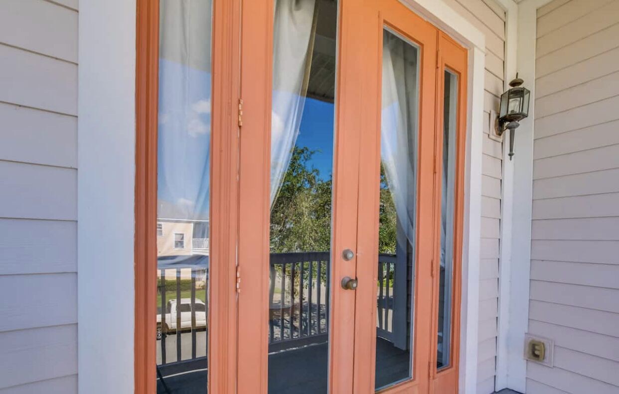 Une porte en bois avec des panneaux de verre, un portail en métal noir et une lanterne fixée au mur.