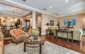 A spacious living room with a fireplace, a dining area, and a kitchen in the background.