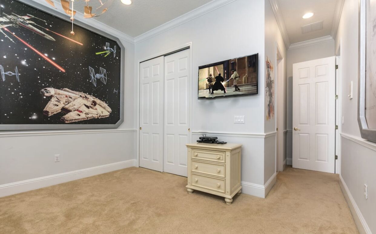 A room with a Star Wars-themed wall mural, a television, a dresser, and white doors.