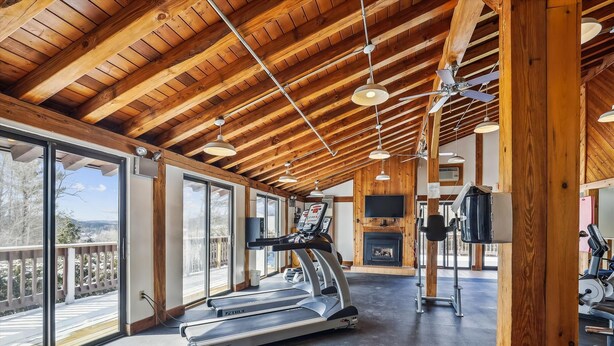 Un gimnasio espacioso con cinta de correr, ventiladores de techo y chimenea.