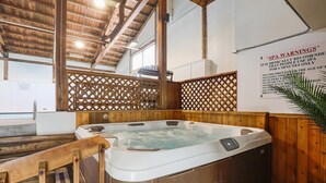 Zona de spa con hidromasaje, vigas de madera y un cartel que enumera las advertencias del spa.