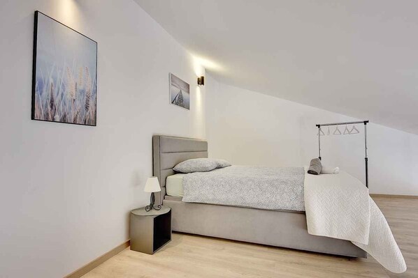 A modern bedroom with a bed, bedside table, lamp, and a hanging light fixture.