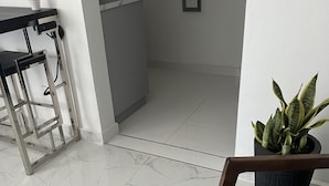 Una cocina moderna con baldosas de mármol blanco, una zona de bar con taburetes y una planta en maceta.