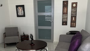 Una sala de estar moderna con un sofá gris, una mesa de centro redonda, un sillón gris y una puerta con paneles de vidrio esmerilado.