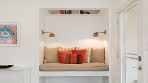 A cozy seating area with a cushioned bench, a small table with a bowl of fruit, and a bookshelf above. - Newly Remodeled Charming and Contemporary Home (Santa Barbara)