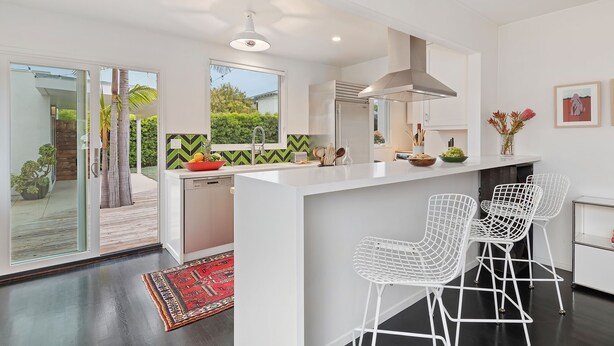 A modern kitchen with a white island, bar stools, and a view of the garden. - Newly Remodeled Charming and Contemporary Home (Santa Barbara)