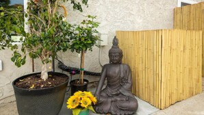 Une statue de Bouddha, deux plantes en pot et une clôture en bambou.