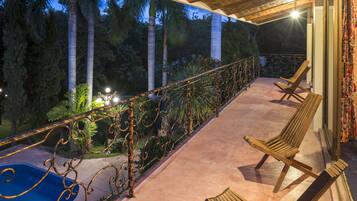 Relax on the balcony overlooking the pool, surrounded by lush greenery and palm trees.