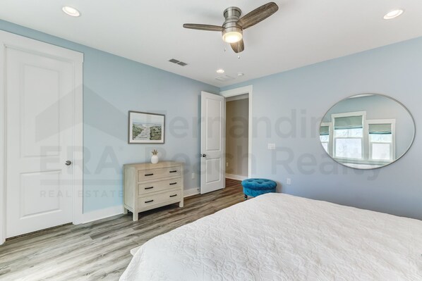 A bedroom with a bed, a dresser, a ceiling fan, and a mirror on the wall.