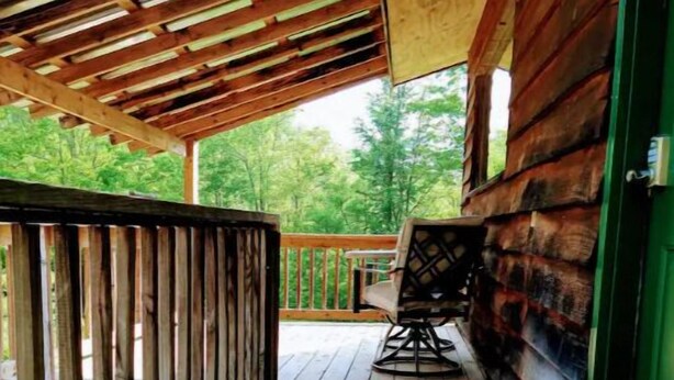 A wooden deck with a wooden railing, a bench, and a welcome mat. - Pondside Cabin (Newland)