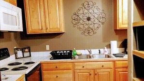 A compact kitchen with wooden cabinets, a white stove, and a decorative wall piece. - Pondside Cabin (Newland)