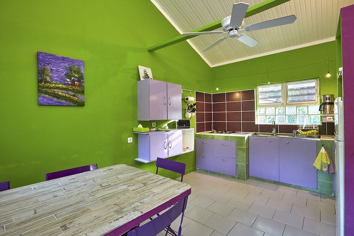 A kitchen with green walls, purple cabinets, and a dining area with a wooden table and chairs.