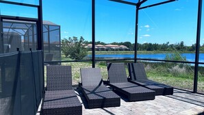 Eine verglaste Terrasse mit Korlounge-Stühlen und Blick auf einen See sowie Gebäude in der Ferne.