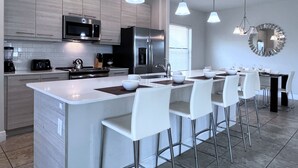 Una cocina moderna con una isla central, taburetes de bar, electrodomésticos de acero inoxidable e iluminación colgante.
