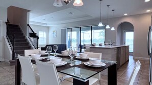 Una cocina moderna con comedor, que incluye una mesa de vidrio, sillas blancas e iluminación colgante.