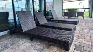 Ein überdachter Außenbereich mit Korlounge-Stühlen und einem Tisch, großen Glasüren und Blick auf ein Wohngebäude.