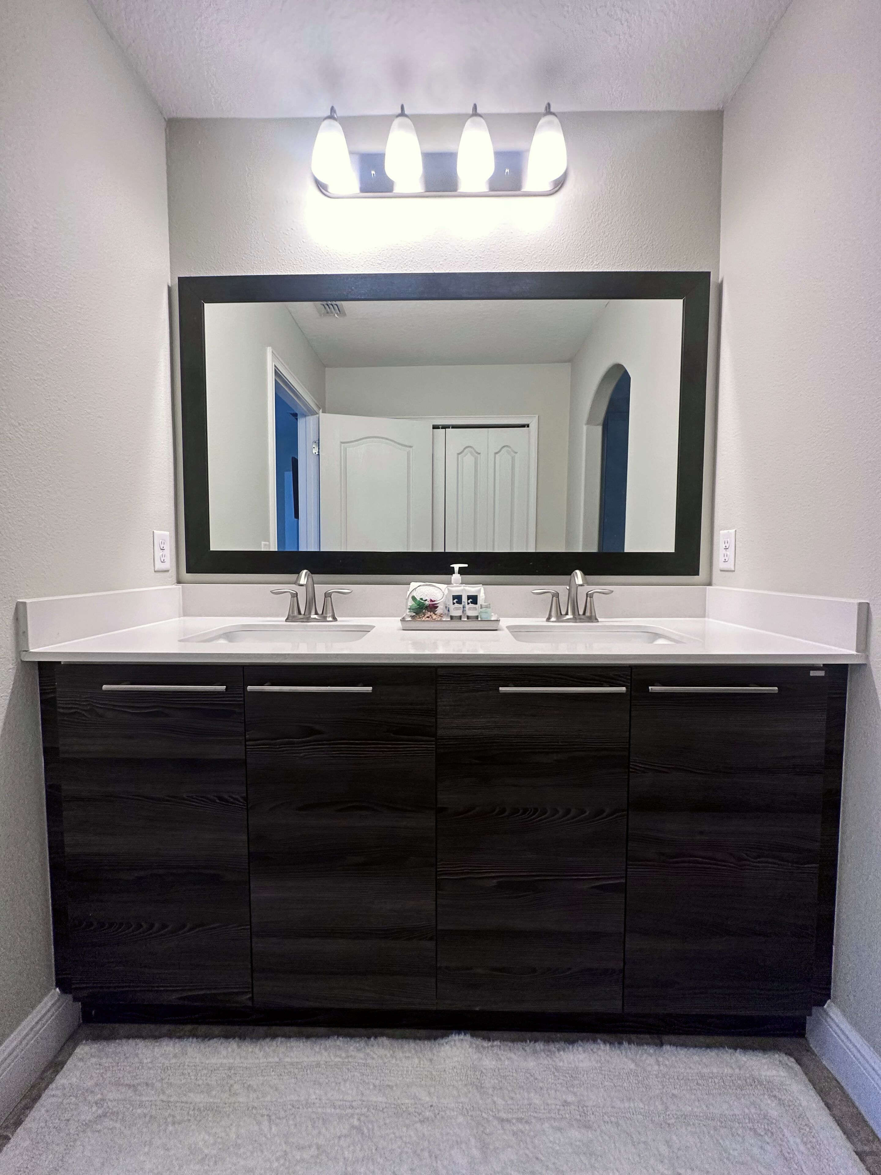 A bathroom with a large mirror, two sinks, dark wood cabinets, and a light-colored countertop.