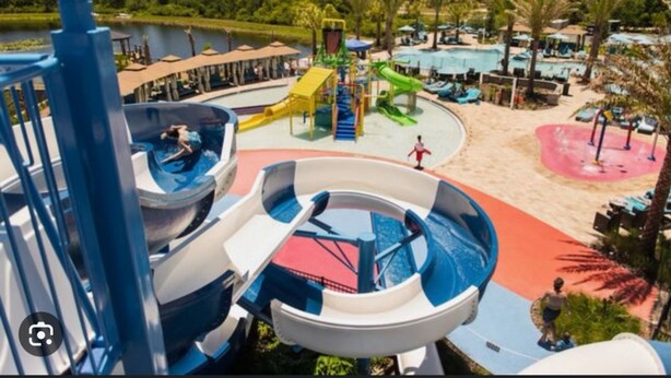 Ein Wasserpark mit mehreren Wasserrutschen und einem Sandbereich mit Sonnenschirmen.