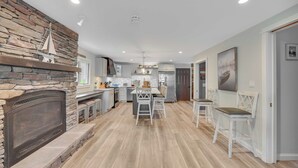 A spacious kitchen with a stone fireplace, wooden flooring, and a central island with seating.