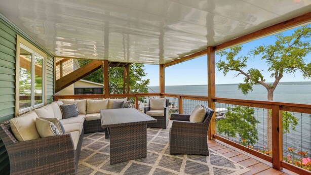 A covered deck with wicker furniture, a table, and a view of the water.