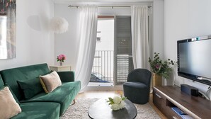 Een moderne woonkamer met een groene bank, een salontafel, een televisie en een balkon met witte gordijnen.