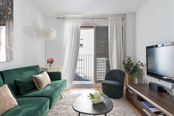 Ein modernes Wohnzimmer mit einem grünen Sofa, einem Couchtisch, einem Fernseher und einem Balkon mit weißen Vorhängen.