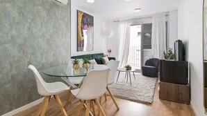 Een moderne woonkamer met een glazen eettafel, witte stoelen, een groene bank en een tv-meubel.