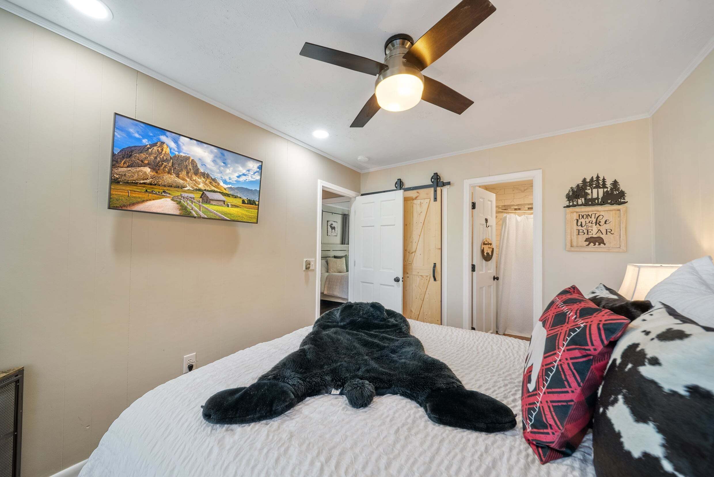 Une chambre à coucher avec un lit, un ventilateur de plafond, une porte et un tableau accroché au mur.