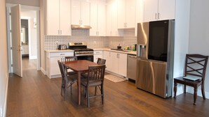 Una cocina moderna con armarios blancos, un refrigerador de acero inoxidable y una mesa de comedor de madera con sillas.