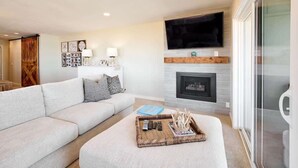 A living room with a sofa, a fireplace, a flat-screen TV, and a glass door leading to a balcony. - Chic Ocean View Condo - Top Floor - Fireplace! (Lincoln City)
