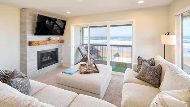 A living room with a fireplace, a television, and a balcony with a view of the ocean. - Chic Ocean View Condo - Top Floor - Fireplace! (Lincoln City)