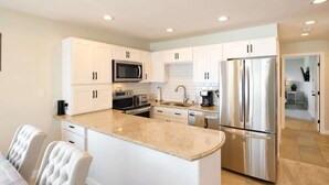 A modern kitchen with white cabinetry, stainless steel appliances, and a marble countertop. - Chic Ocean View Condo - Top Floor - Fireplace! (Lincoln City)