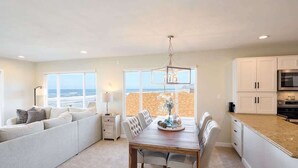 A modern kitchen with a view of the beach, a dining area with a table and chairs, and a seating area with a sofa. - Chic Ocean View Condo - Top Floor - Fireplace! (Lincoln City)