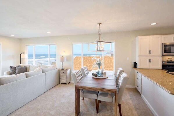 A modern kitchen with a view of the beach, a dining area with a table and chairs, and a seating area with a sofa.