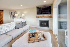 A living room with a sofa, a fireplace, a television, and a tray with remote controls.