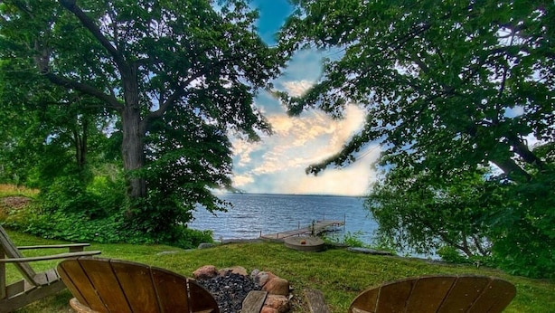 A lakeside seating area with two wooden Adirondack chairs and a fire pit. - Historic Loyalist Lakehouse • Quiet Waterfront Escape • 3.5 Acres & 300’ Shore! (Prince Edward)